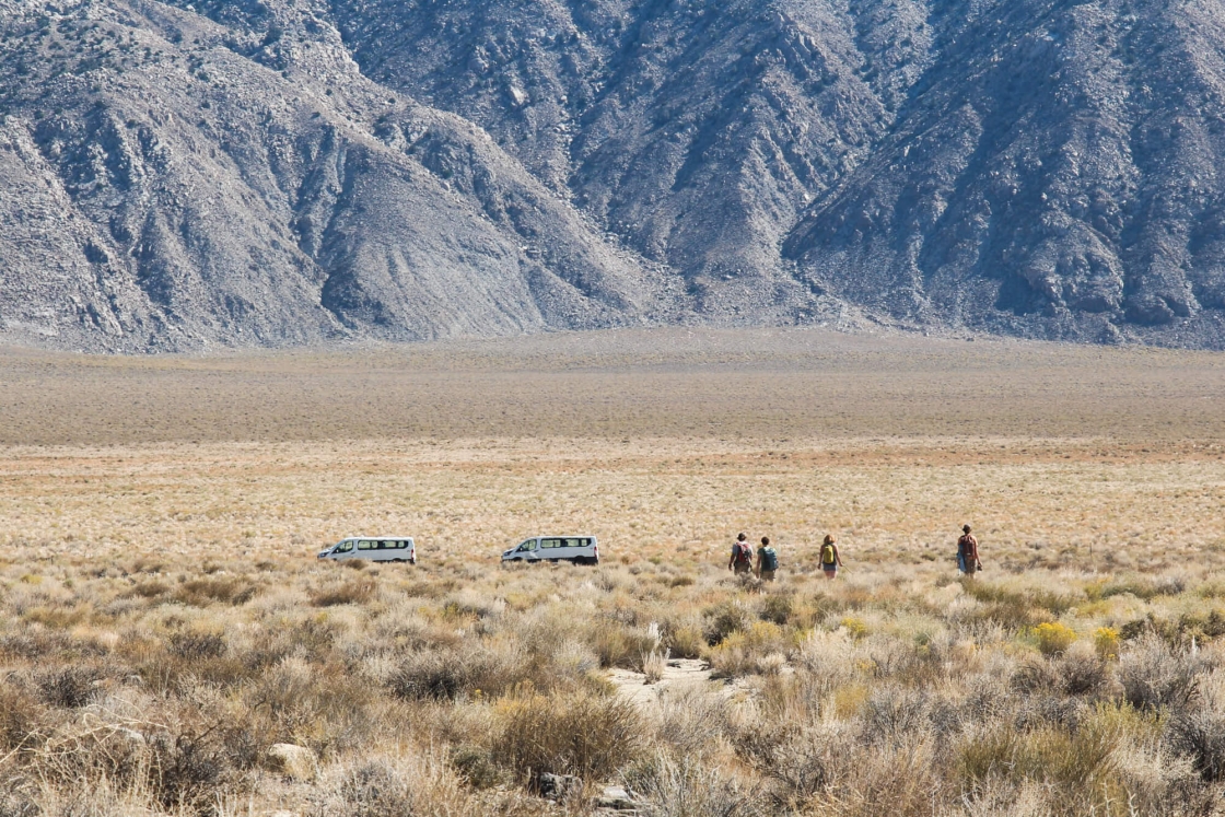 Students walking through a field in Deep Springs Valley, Calif. toward 2 white vans.