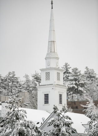 A church steeple surrounded by snow covered pines