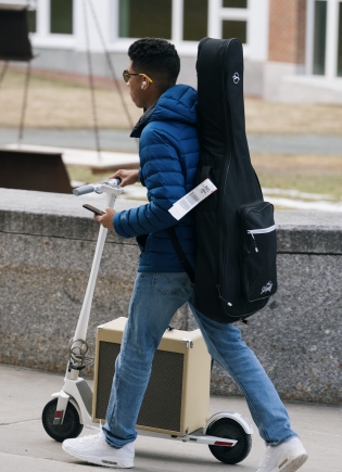 Student transports his instruments on a scooter.