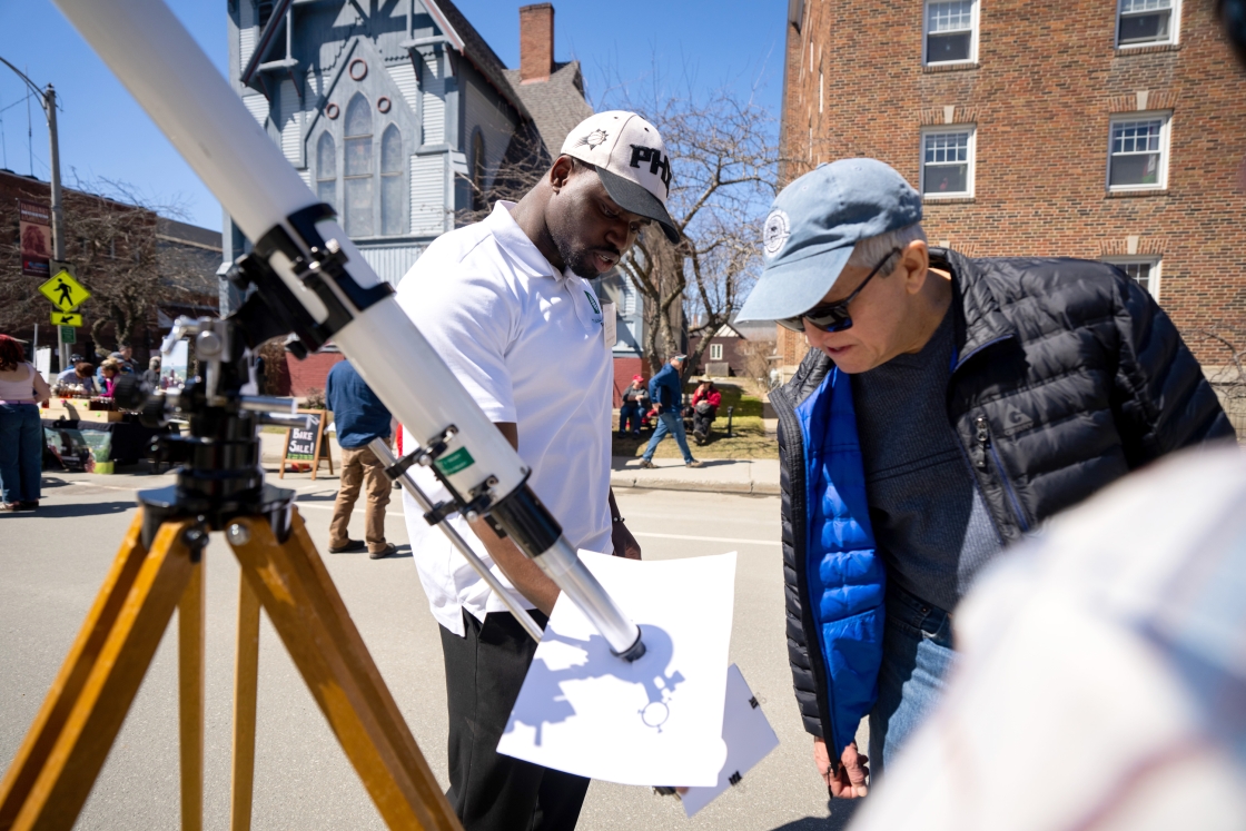 Emmanuel Durodola, Guarini '25, and a on-looker examine a telescope