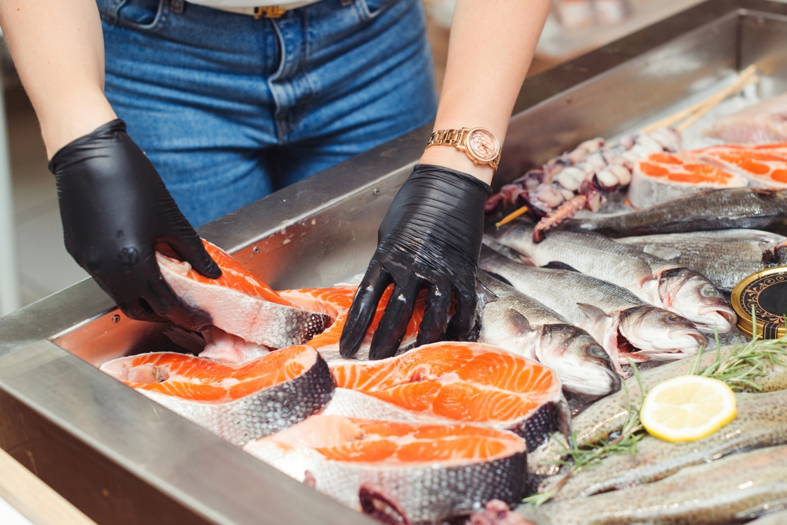 Person wearing black gloves laying out seafood