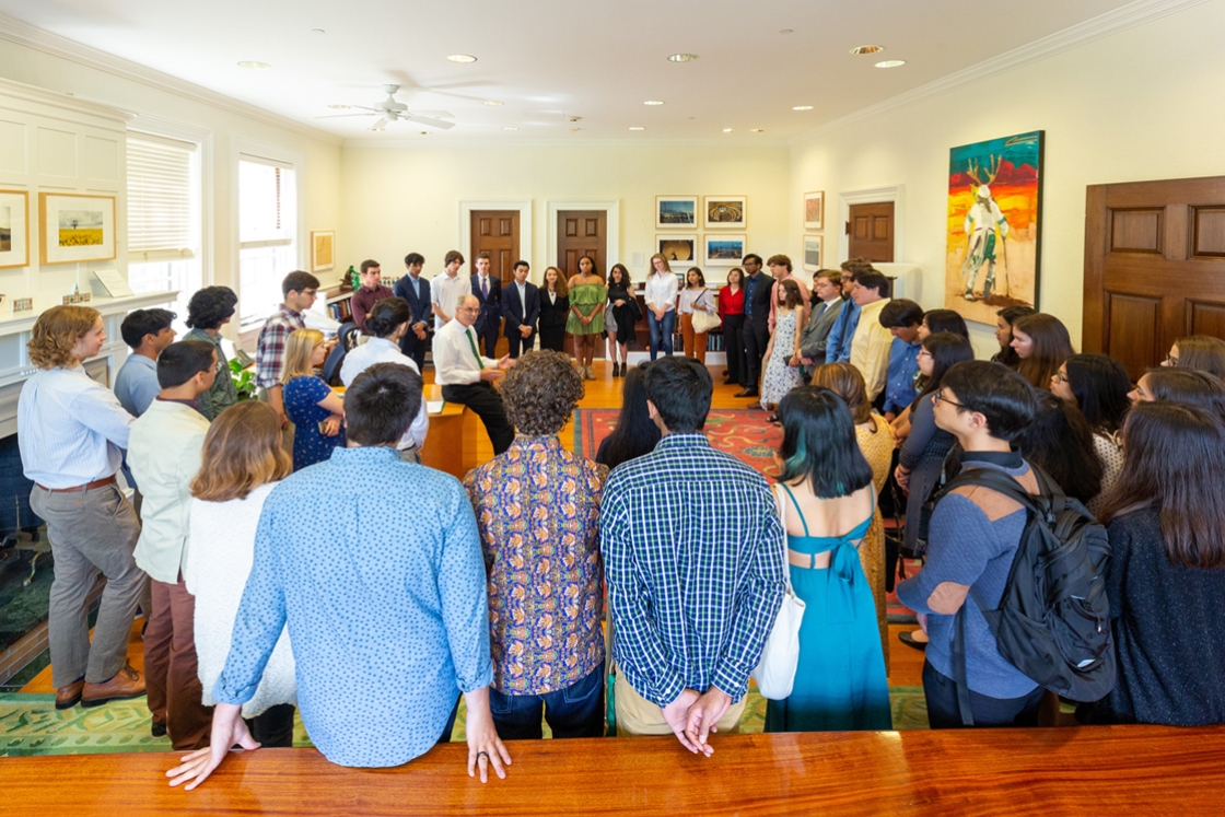 A group of students stands in a circle listening to President Philip J. Hanlon '77 speaking in his office.