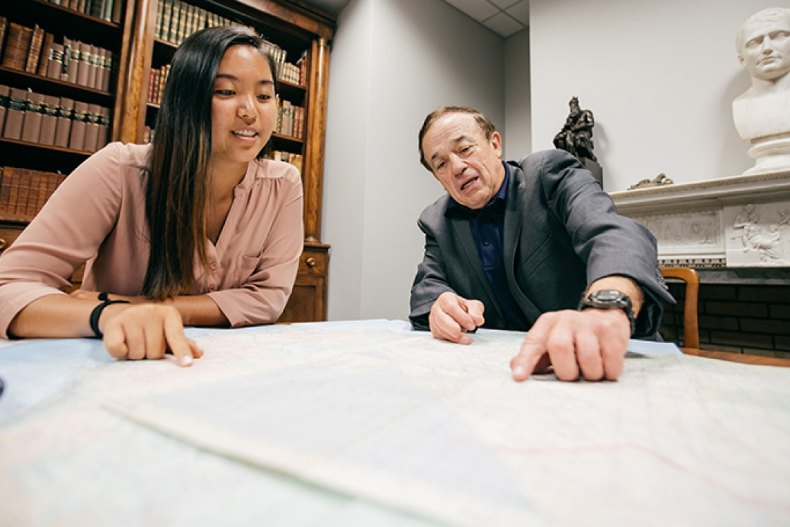a student and professor examining a map spread out on a table