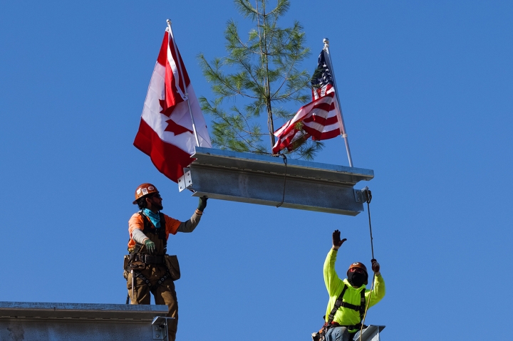 Culminating the topping-off ceremony, workers lower the beam into place.