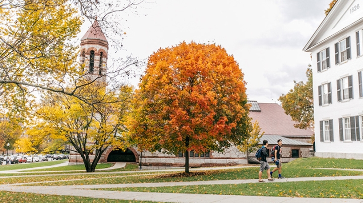 Two students walk to Dartmouth Hall in the fall with Rooke Chapel in the background